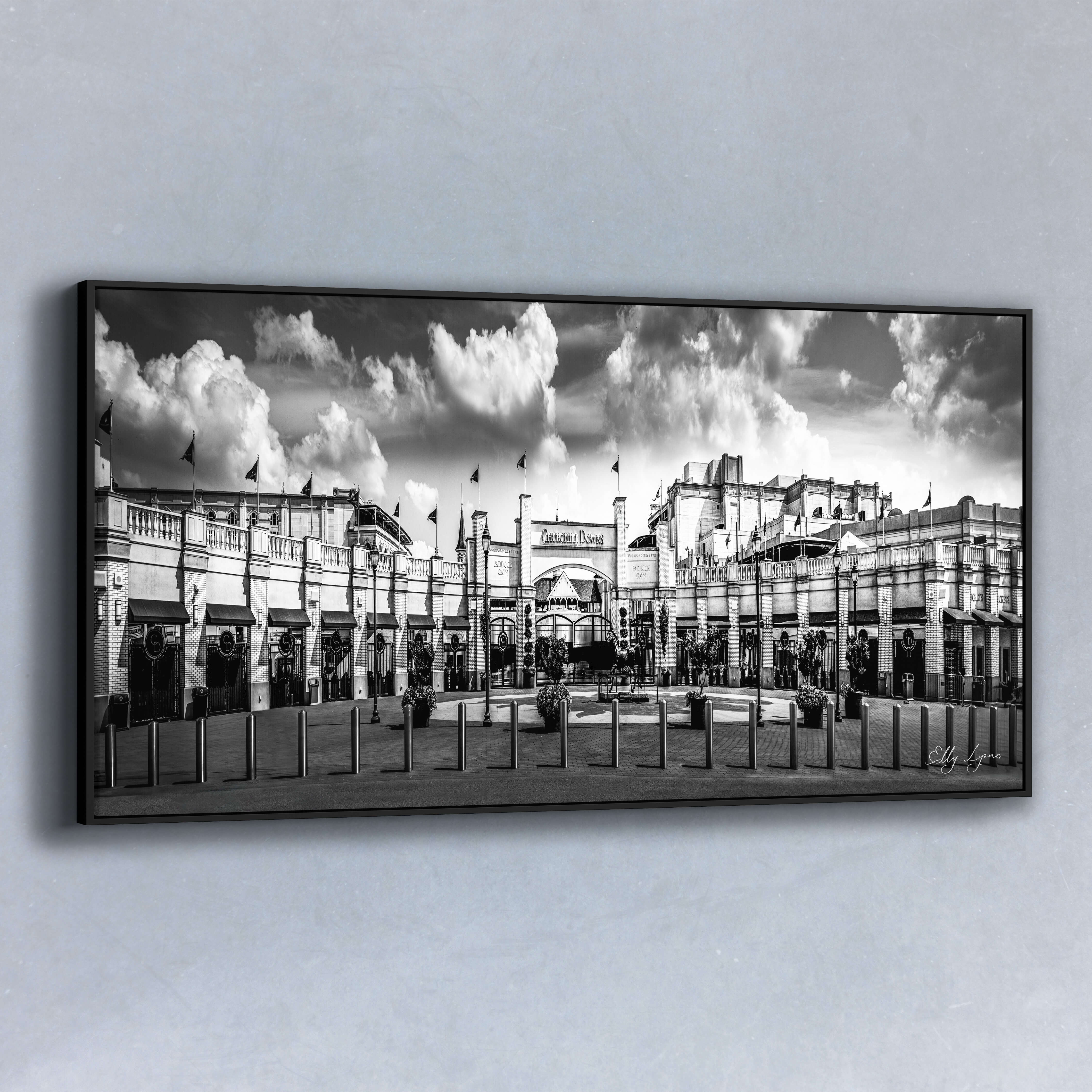 Panoramic black and white fine art photo of the grand entrance of Churchill Downs featuring dramatic clouds, flags, and historic architecture.