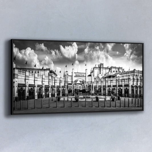 Panoramic black and white fine art photo of the grand entrance of Churchill Downs featuring dramatic clouds, flags, and historic architecture.